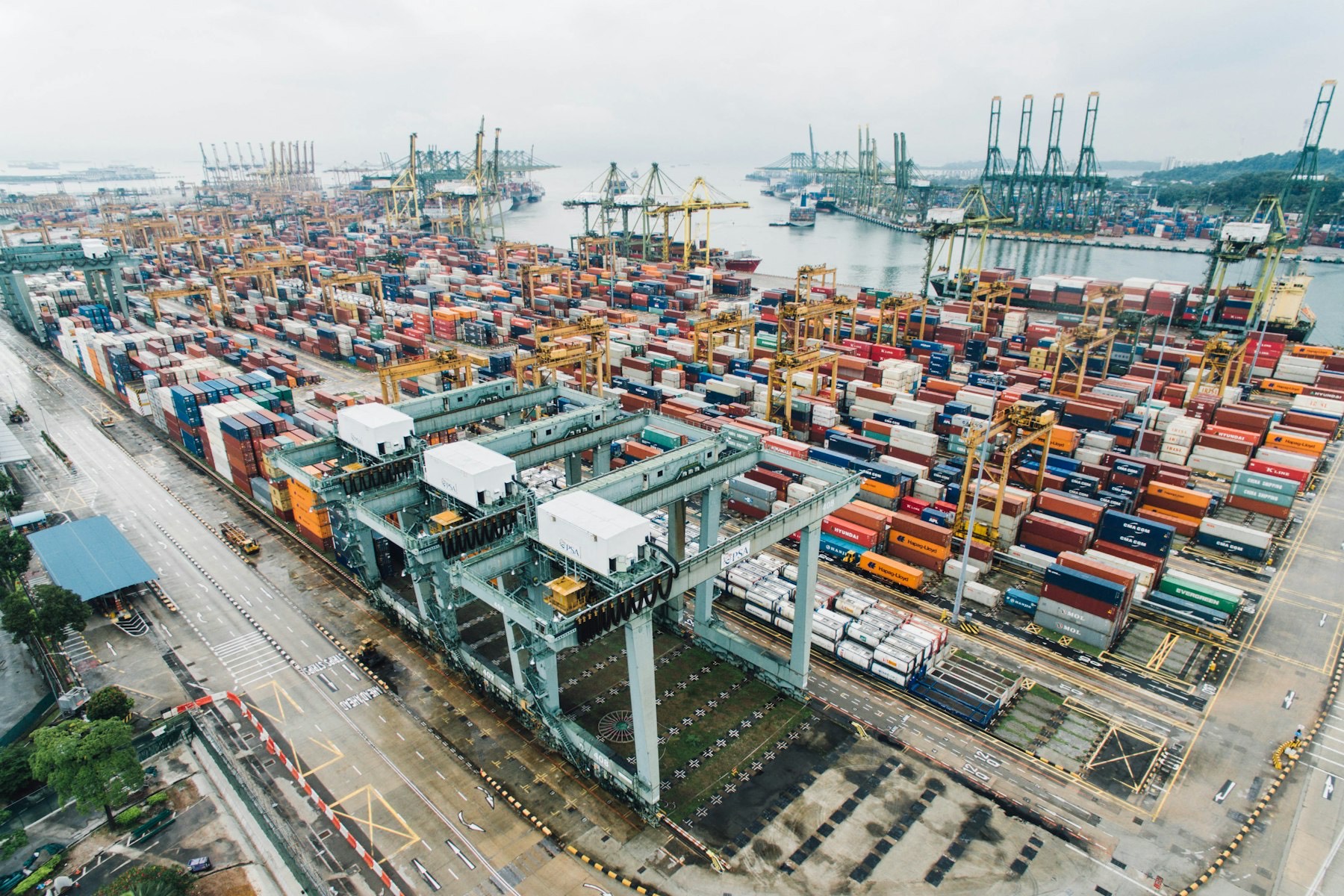 Aerial view of a container terminal: straddle carriers, stacked containers and quay cranes in overcast light