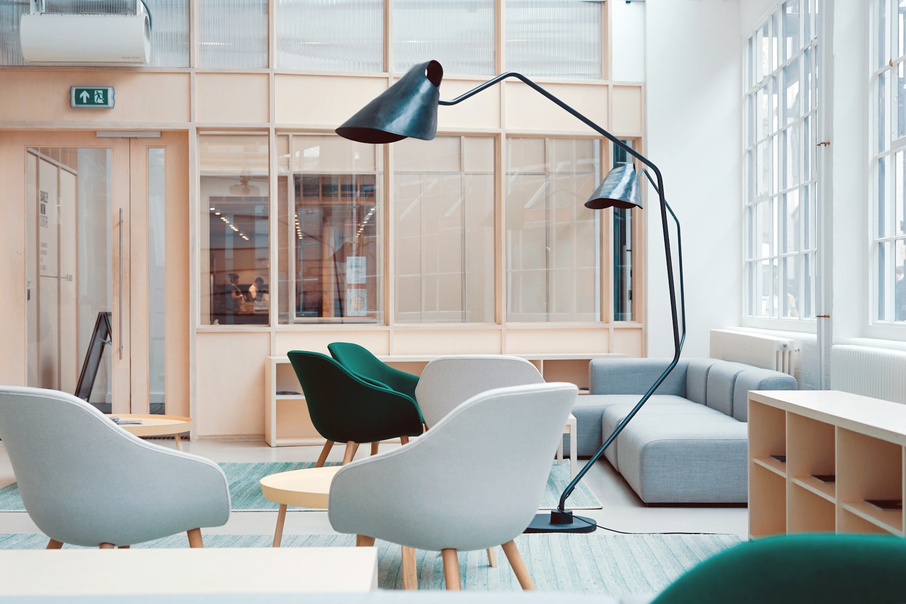 A pale meeting room with two deep green armchairs and a black floor lamp.
