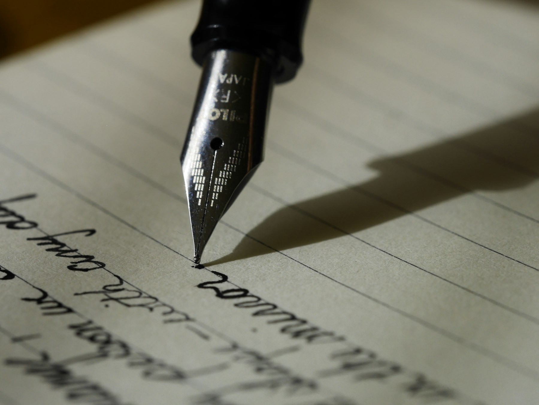 A fountain pen nib at rest on a handwritten page, in low raking light.